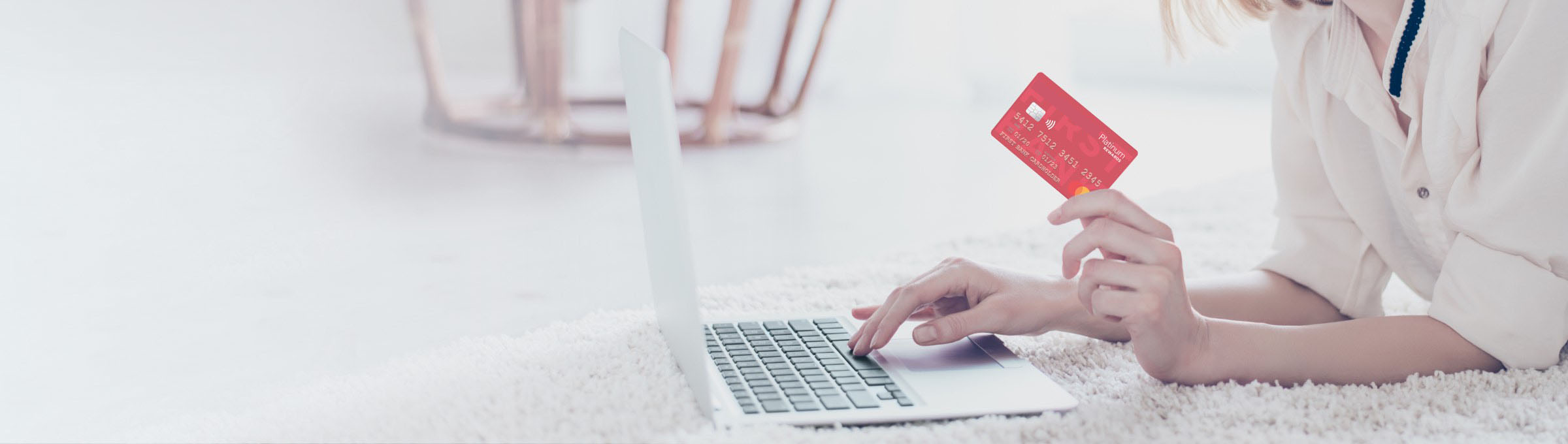 a woman holding her Highridge Credit Union Platinum Rewards card while on the computer.